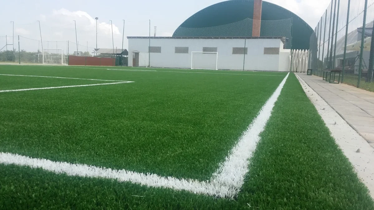 Fudbalski teren sa veštačkom travom i belim linijama, sa balon halom u pozadini