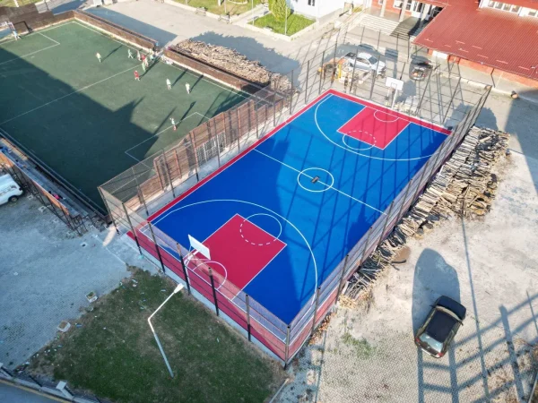 Snimak iz vazduha plavo-crvenog košarkaškog terena sa reflektorima