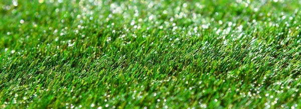 Površina veštačke trave sa kapima rose u jutarnjem svetlu